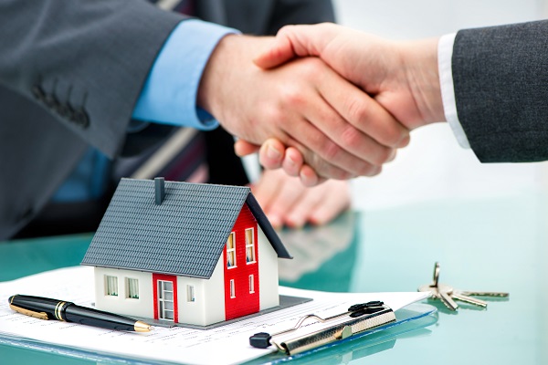 Two men shaking hands over a house model