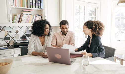 Three people at a dining room table looking over documents with a laptop open