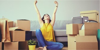 an excited woman with her hands up sitting on the floor surrounded by boxes