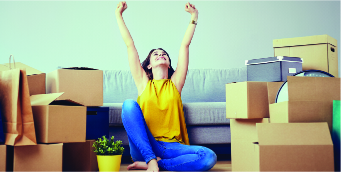 an excited woman with her hands up sitting on the floor surrounded by boxes