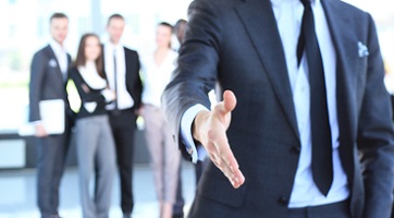 A man reaching his hand out for a handshake and a group of blurred out people in the background 